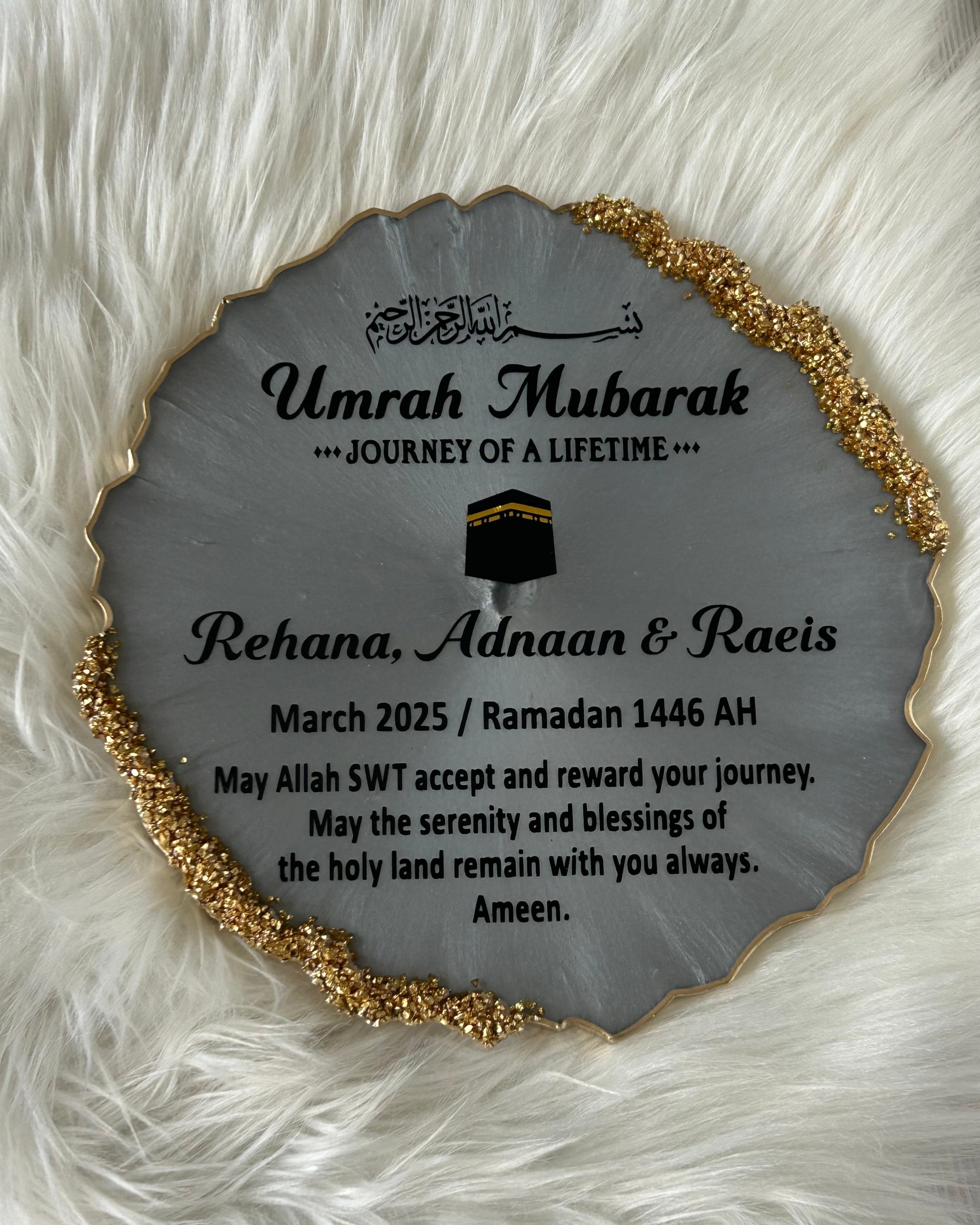 Decorative plaque with black Umrah Mubarak text on a fluffy white surface