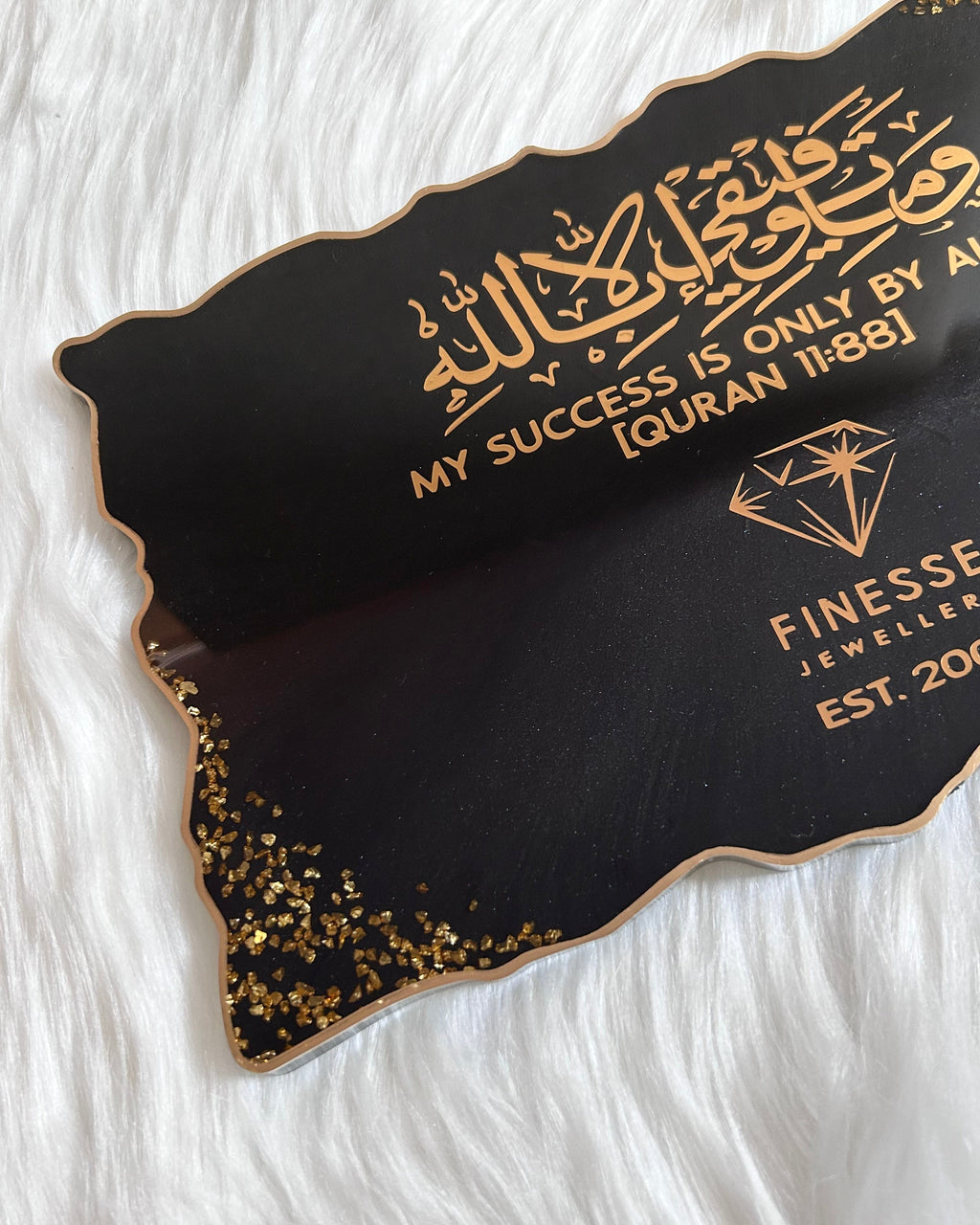 Black and gold personalised business branding plaque/tray with business logo and quran verse 11:88 written in gold on a white fur background background