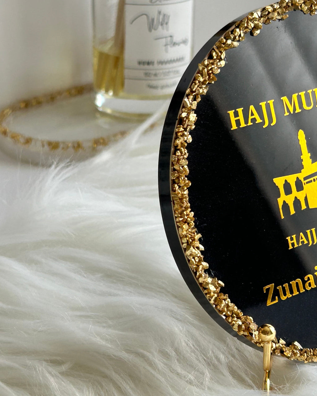 Round black decorative Hajj Mubarak plaque with gold rim and text on a white surface with decorative elements.