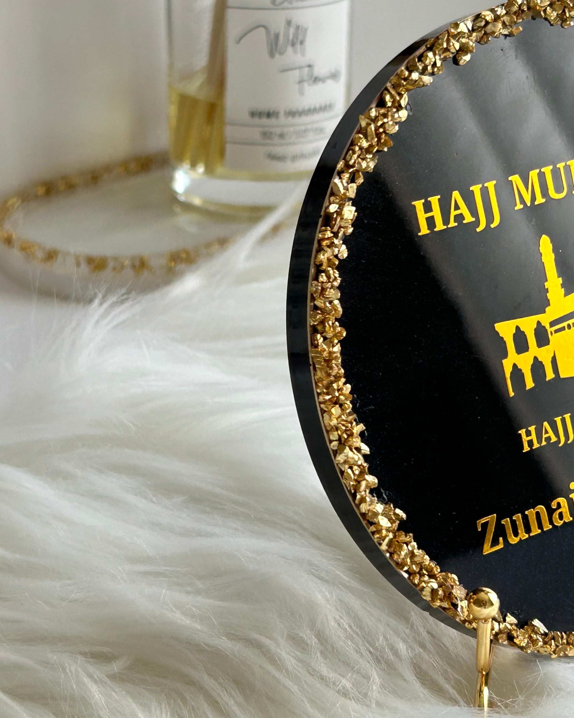 Round black decorative Hajj Mubarak plaque with gold rim and text on a white surface with decorative elements.
