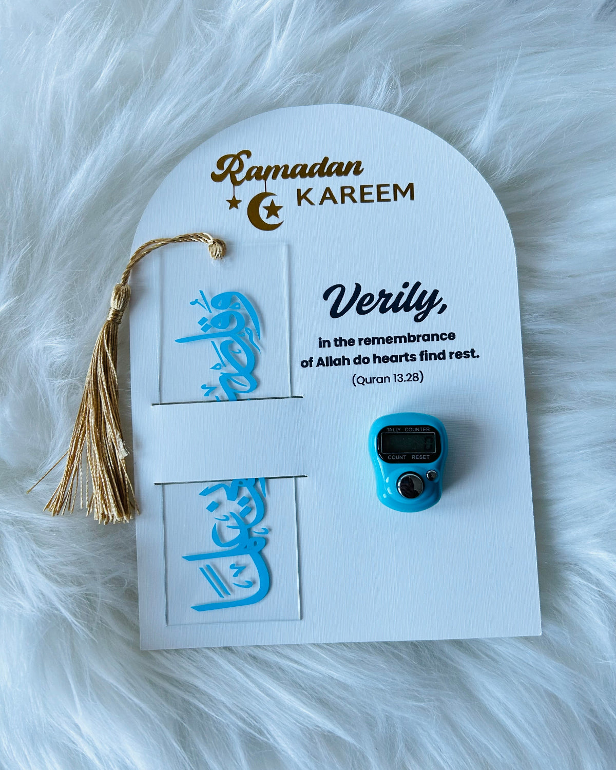 A gift set for Ramadan displayed on a white background, including a blue and gold acrylic bookmark, a blue and silver Counter Tasbeeh, and a greeting card with a quote from the Quran.