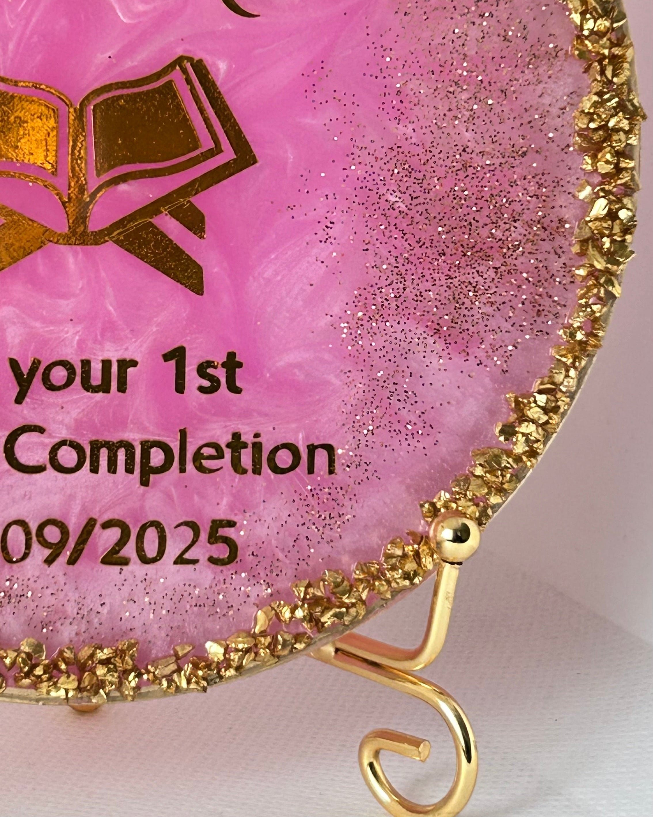 Decorative Quran completion plaque with gold text and design on a pink background