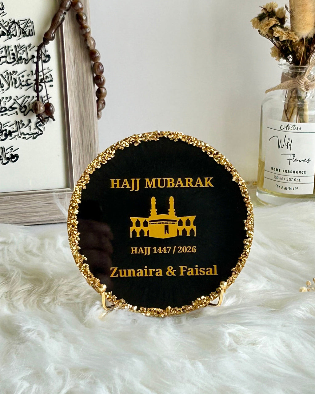Round black decorative Hajj Mubarak plaque with gold rim and text on a white surface with decorative elements.