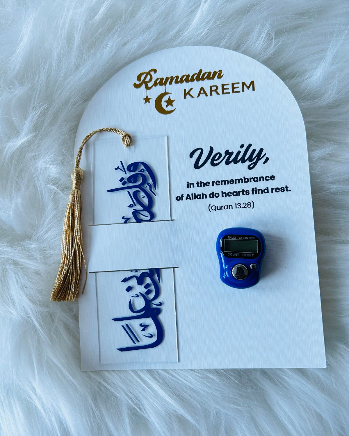A gift set for Ramadan displayed on a white background, including a black and gold acrylic bookmark, a black and silver Counter Tasbeeh, and a greeting card with a quote from the Quran.