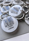 QR code with business name on in black colour on a white round resin keyring with a silver chain.