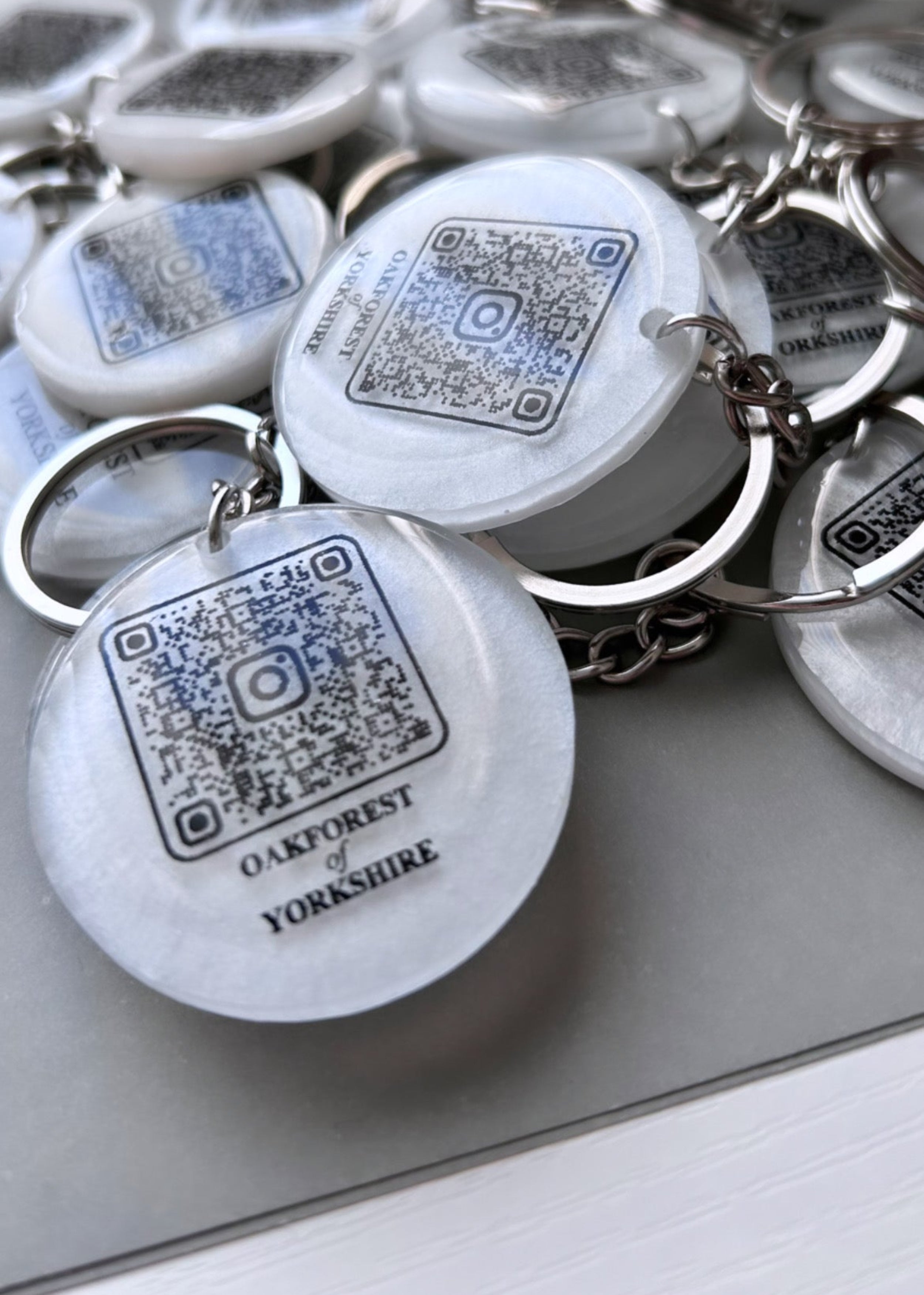 QR code with business name on in black colour on a white round resin keyring with a silver chain.