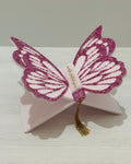 Pink butterfly-shaped Quran holder stand with wings decorated with pink glitter and matching bookmark on a white surface