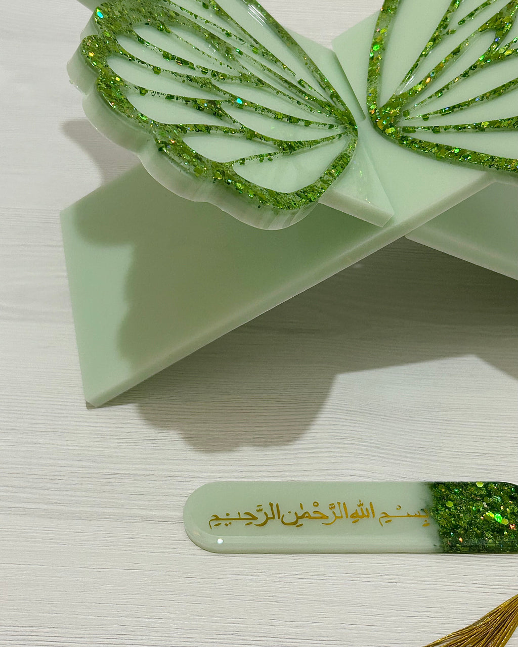 Green decorative butterlfy shaped Quran holder stand with glittery details on the wings with a matching bookmark on a white background
