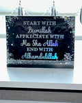 Decorative banner with Arabic text on a black background with glitter, hanging against a window.