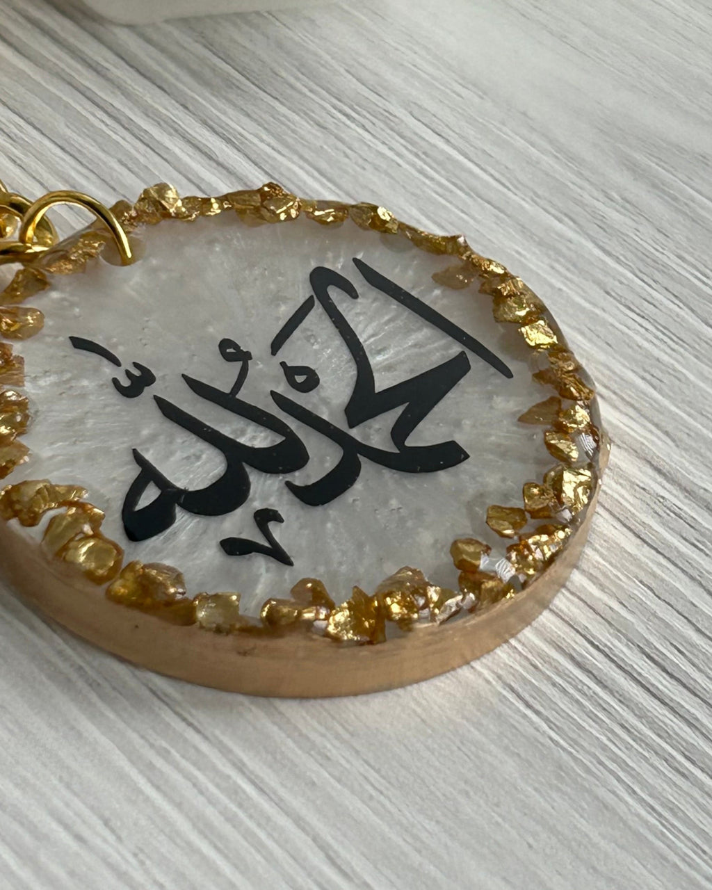 Decorative keychain with Arabic text on a white surface with a white rose.