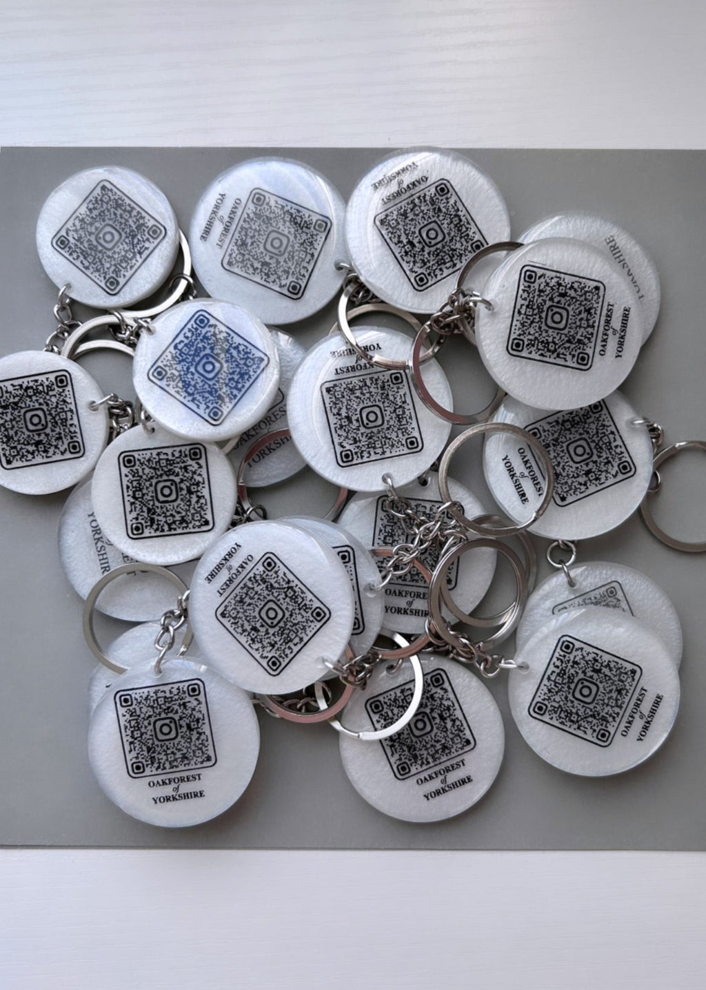white colour round resin keyring with a business name and QR code link to their website in black colour with a silver chain on a grey backgroung