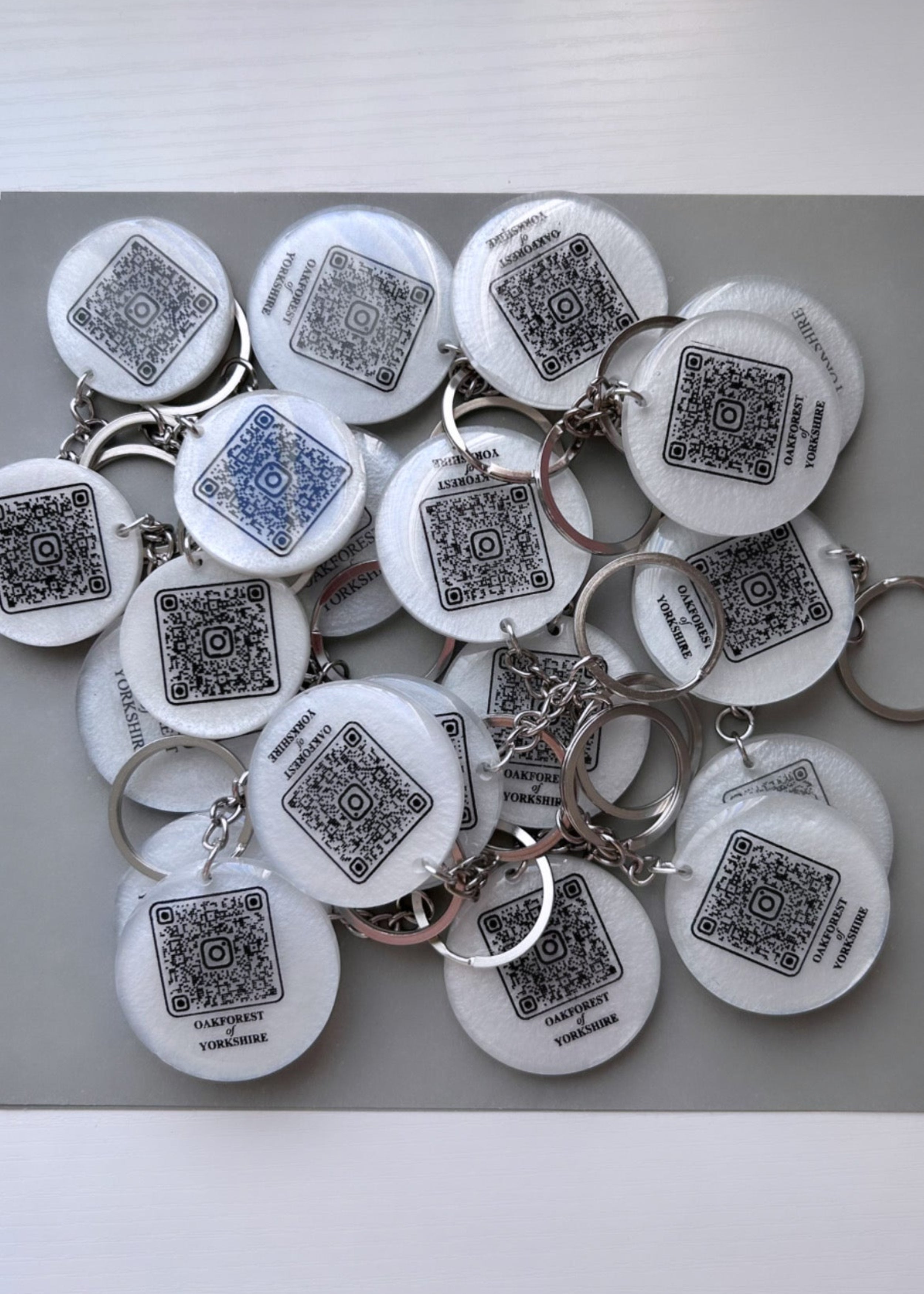 white colour round resin keyring with a business name and QR code link to their website in black colour with a silver chain on a grey backgroung