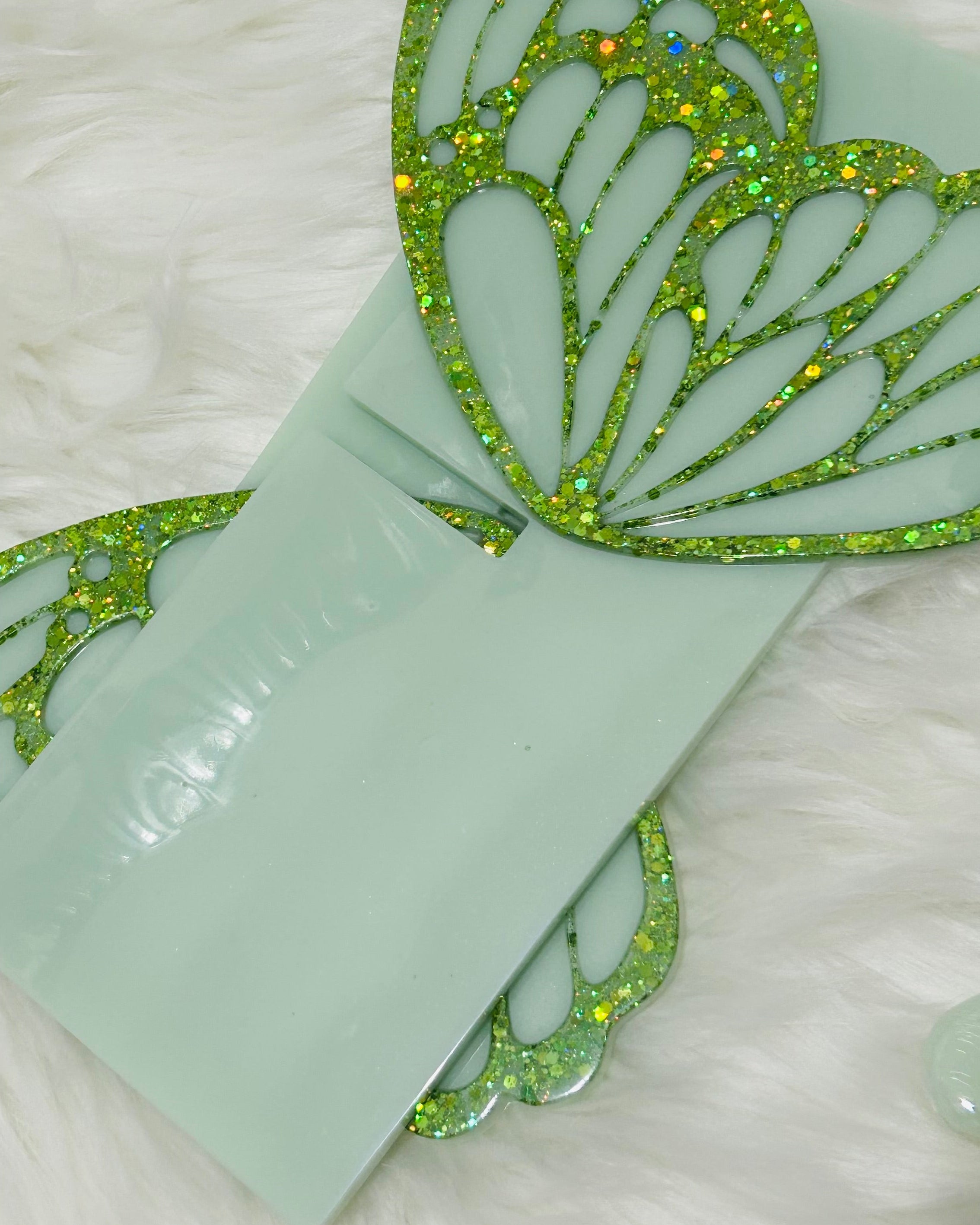Sage green butterfly Quran stand holder with green glittery butterfly wings on a white textured fur background