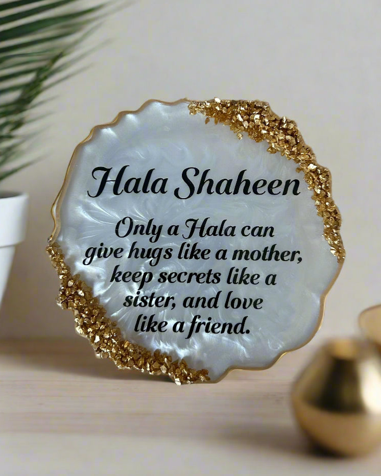 Decorative plate with 'Hala Shaheen' quote on a white surface with red petals and gold decorative elements.