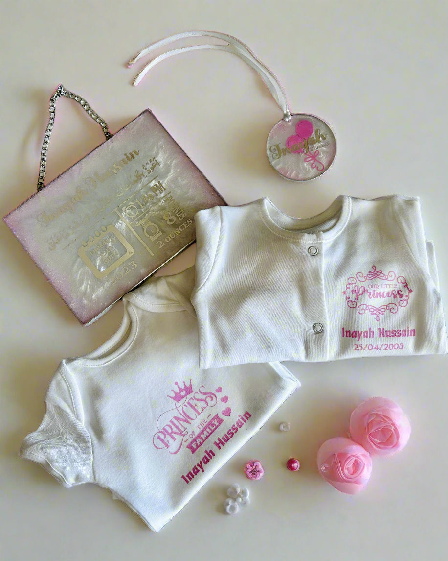 Baby clothing set with 'Princess' and name print, including a personalised resin baby birth details plaque with a chain to hang on the wall with and name ornament on a light background.