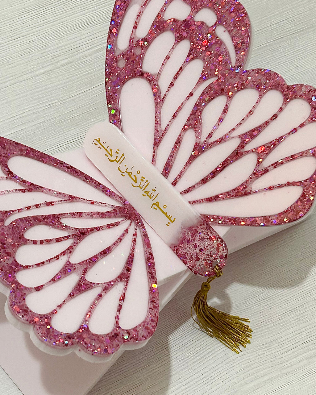 Butterfly-shaped Quran book holder stand with pink glitter wings and a bookmark with gold tassel on a white background
