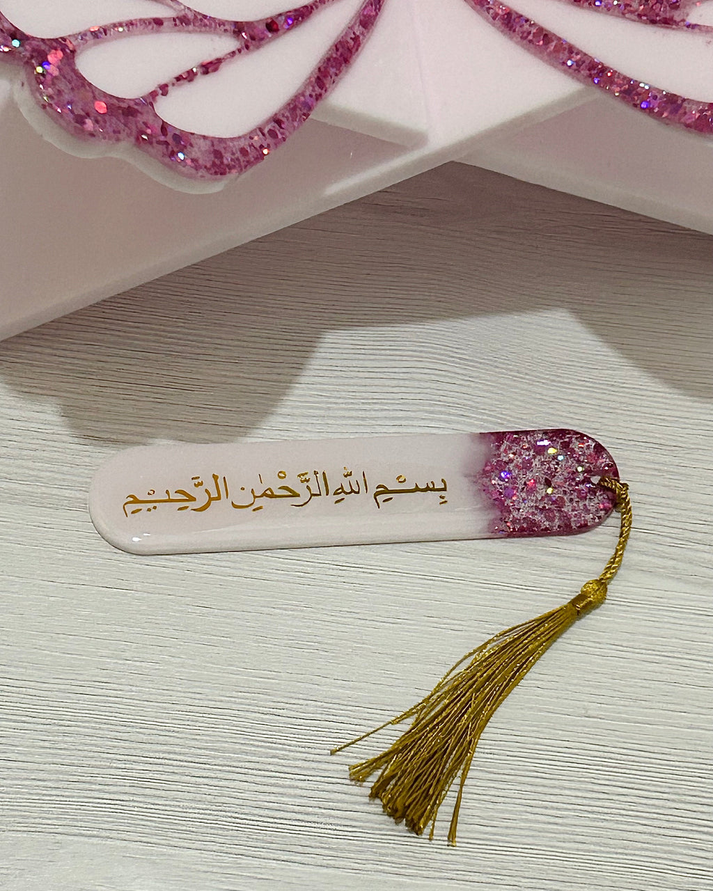 Decorative bookmark with Arabic text, glittery design, and tassel on a textured surface.