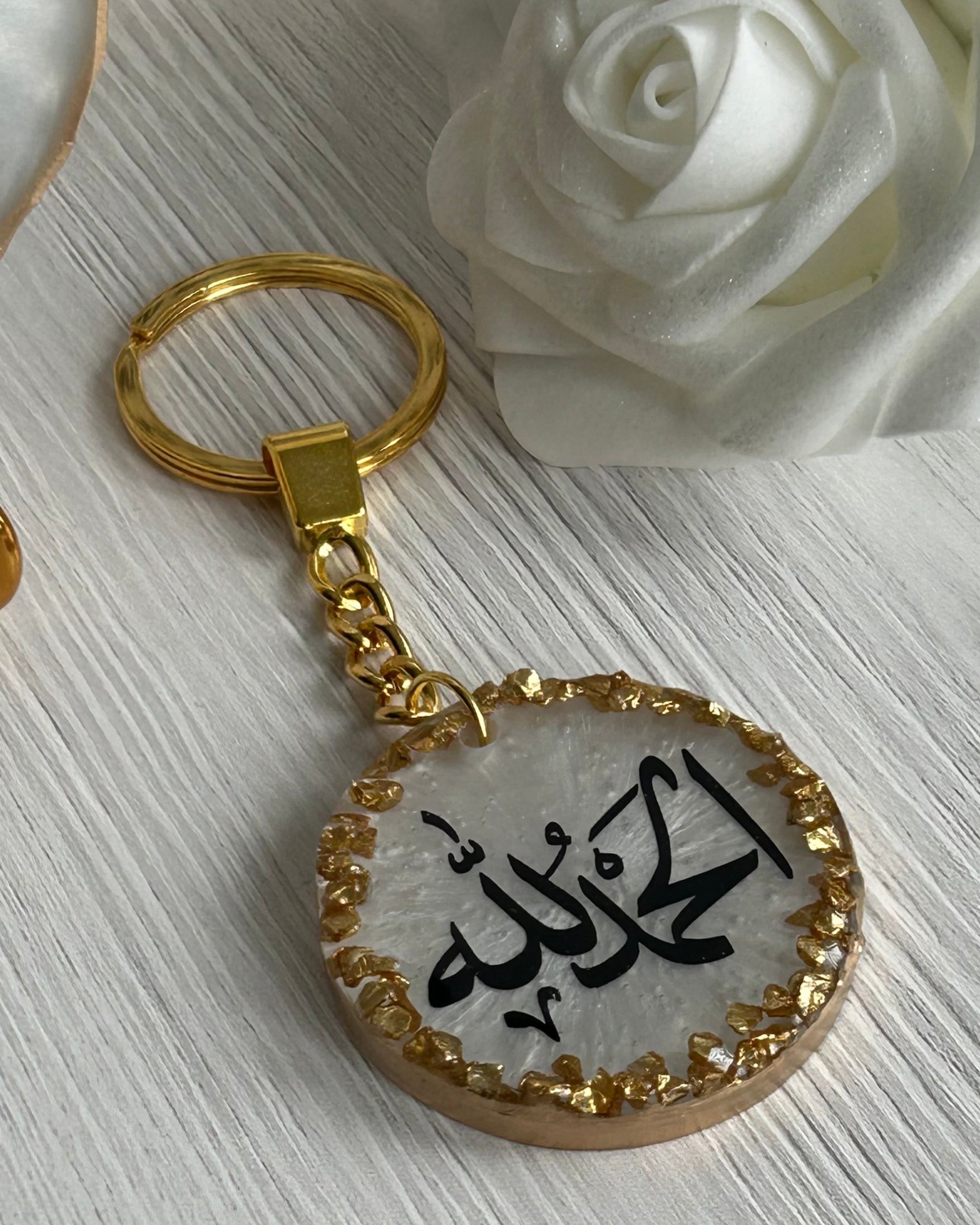 Gold keychain with Arabic text on a white surface