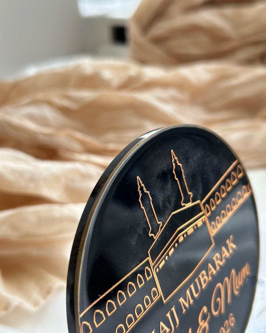 Decorative plate with Arabic text and a silhouette of a mosque, placed on a surface with a blurred background.