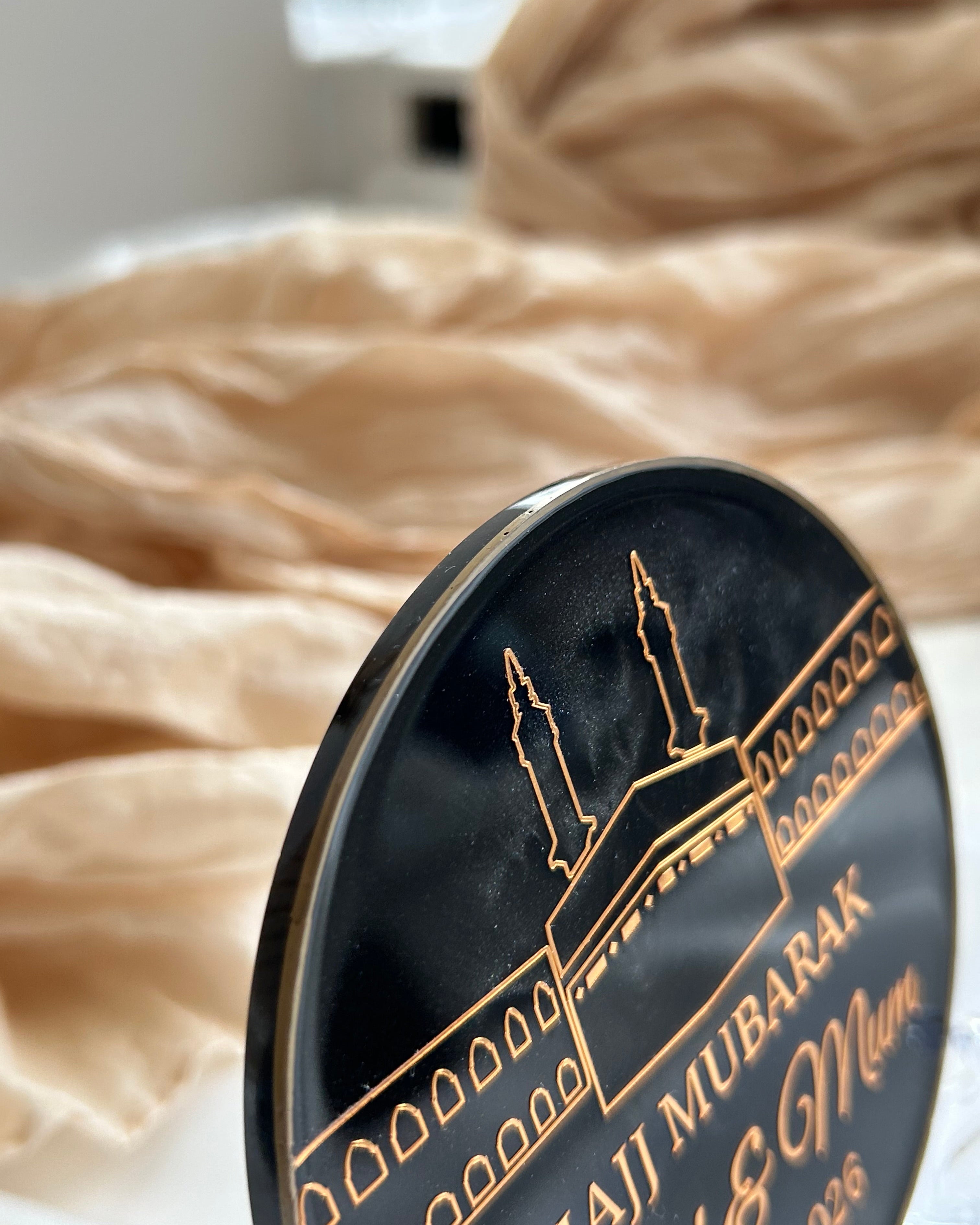 Decorative plate with Arabic text and a silhouette of a mosque, placed on a surface with a blurred background.