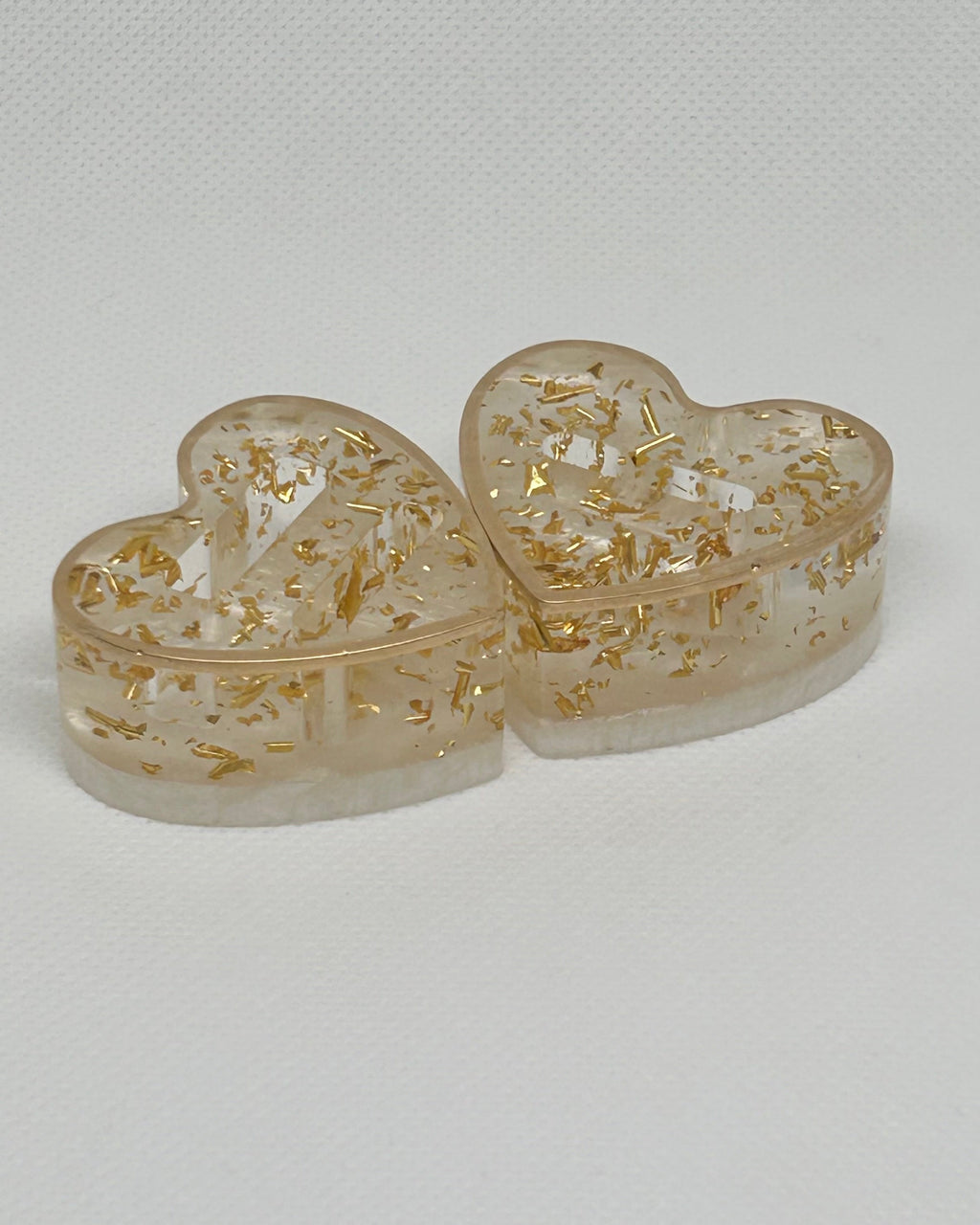 Heart-shaped transparent containers with gold floral designs on a light gray background
