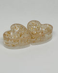 Heart-shaped transparent containers with gold floral designs on a light gray background