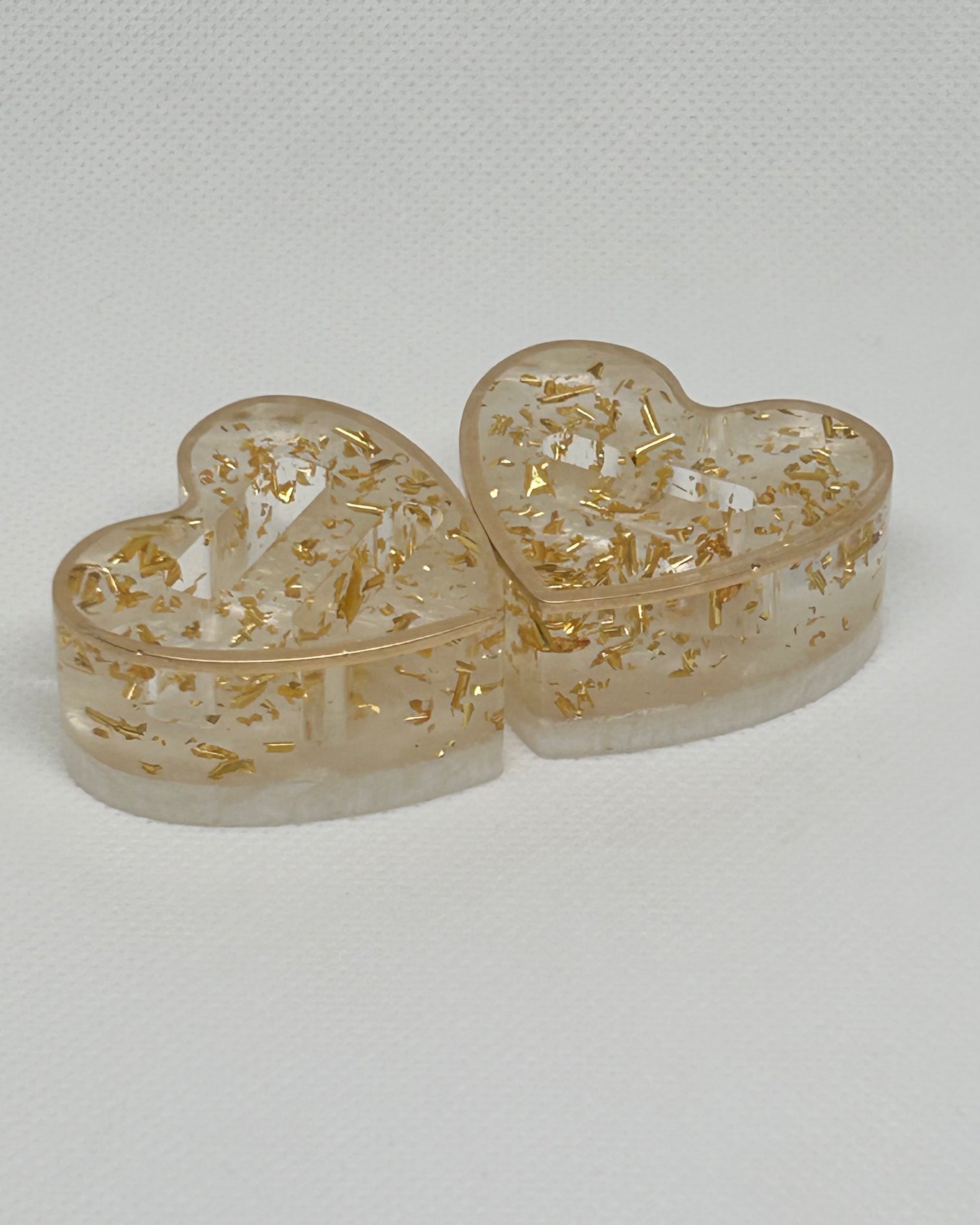 Heart-shaped transparent containers with gold floral designs on a light gray background