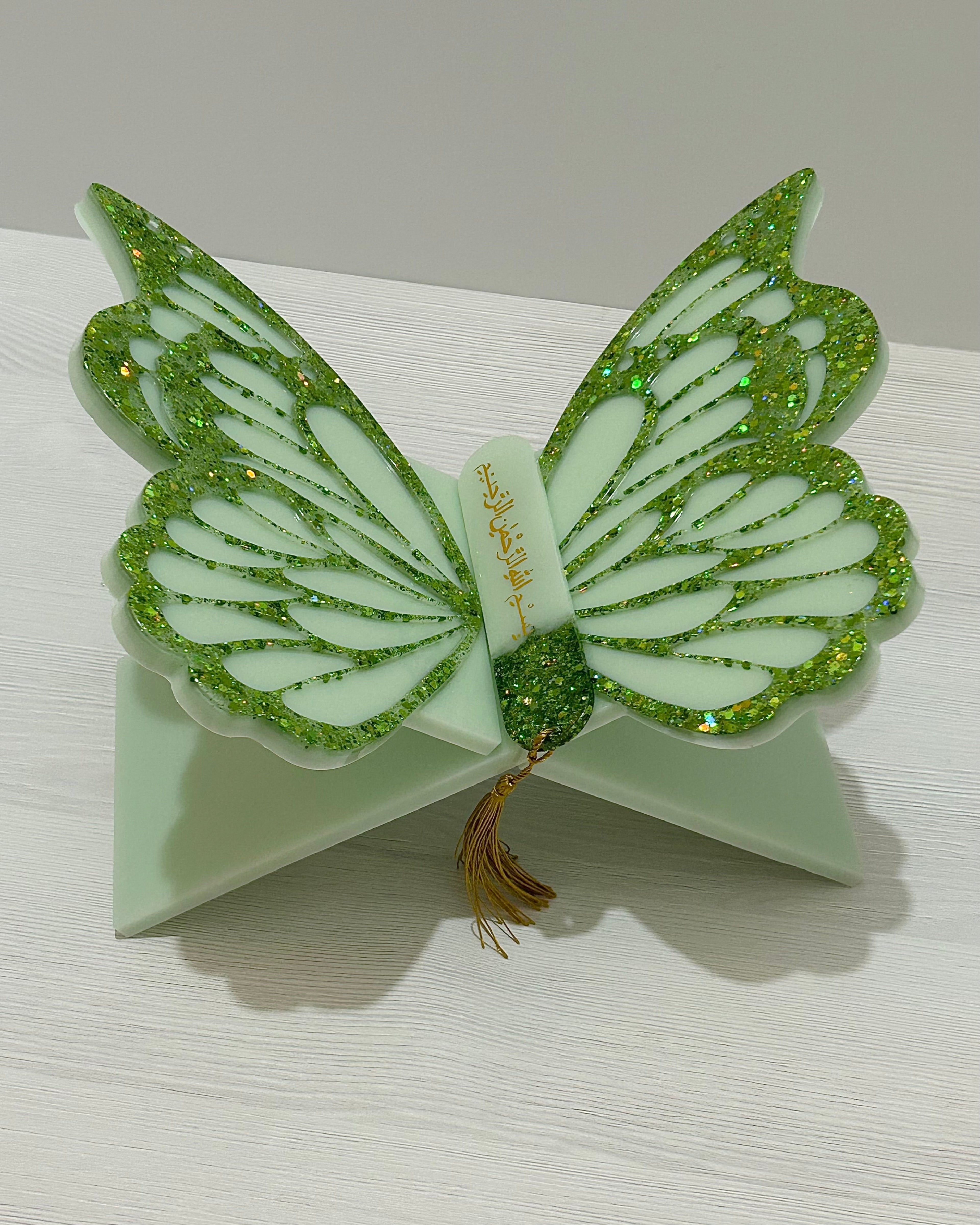 Green butterfly-shaped Quran holder stand decorated with green glitter and matching bookmark on a white surface