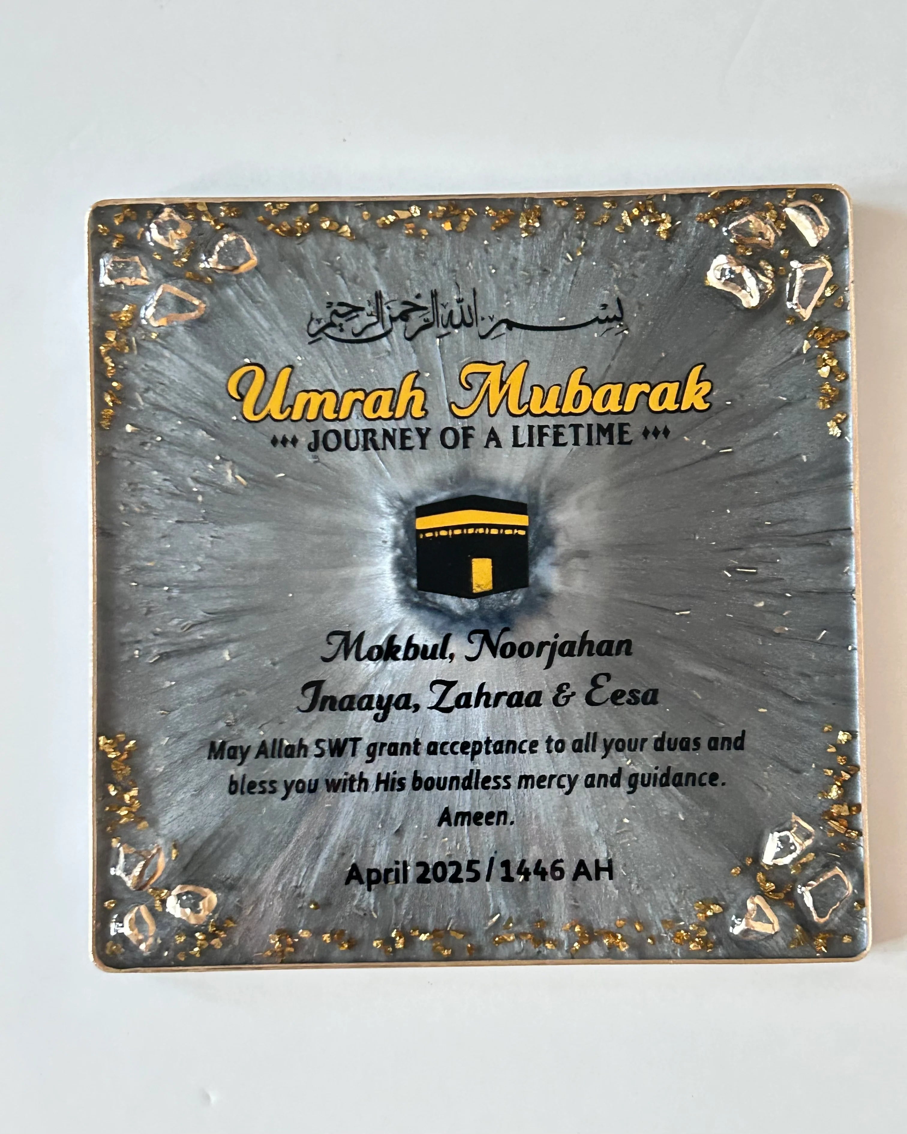 Decorative plaque with 'Umrah Mubarak' text and a graphic of the Kaaba on a gray background.