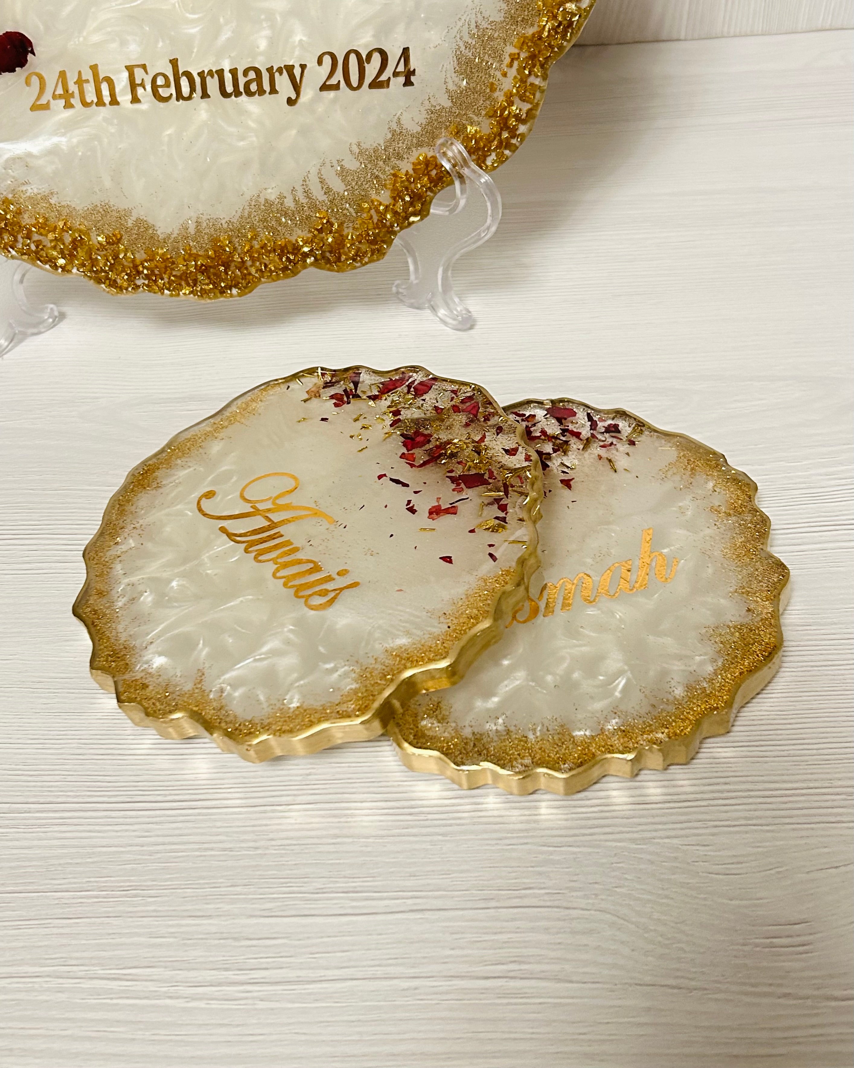 Decorative coasters personalised with couples names with gold edge on a white surface.