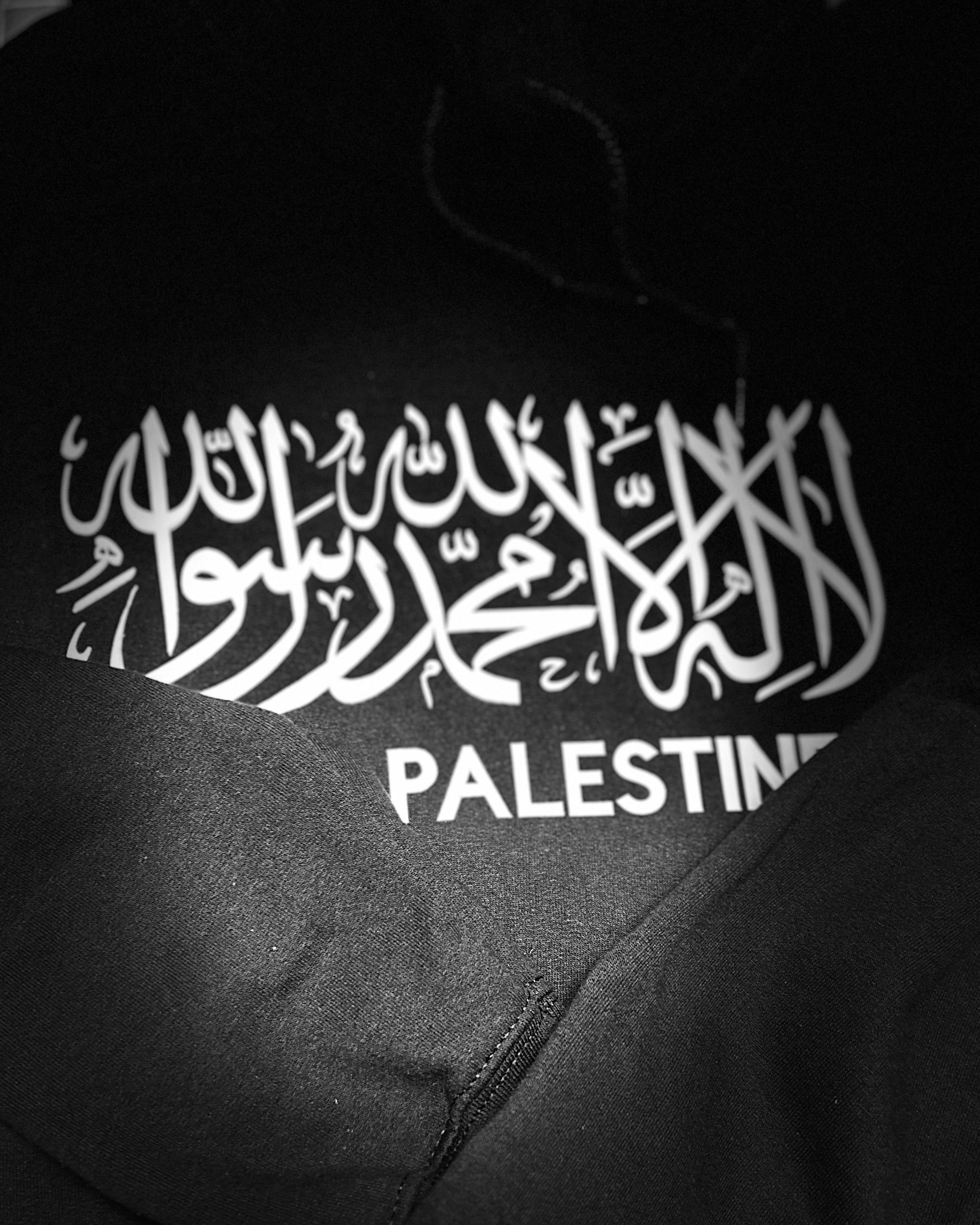 Black garment with white Arabic text and 'PALESTINE' printed below on a black background