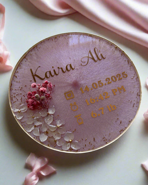 Decorative resin baby announcement plate with gold personalised text and floral design on a fluffy white surface 
