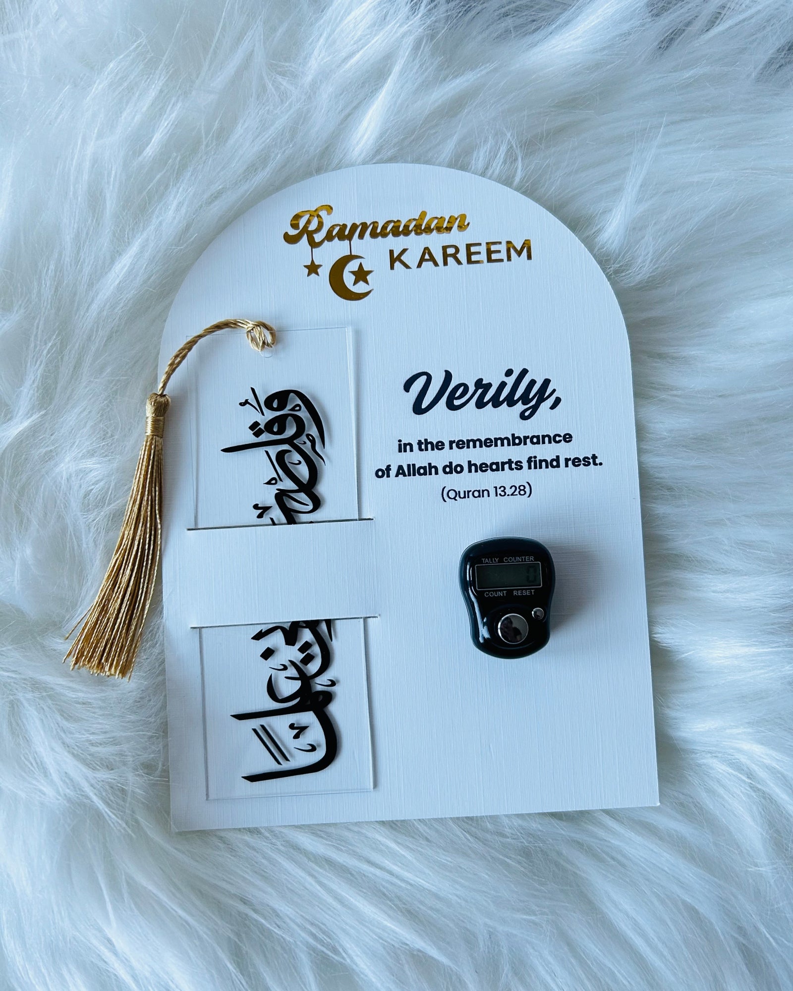 A gift set for Ramadan displayed on a white background, including a black and gold acrylic bookmark, a black and silver Counter Tasbeeh, and a greeting card with a quote from the Quran.