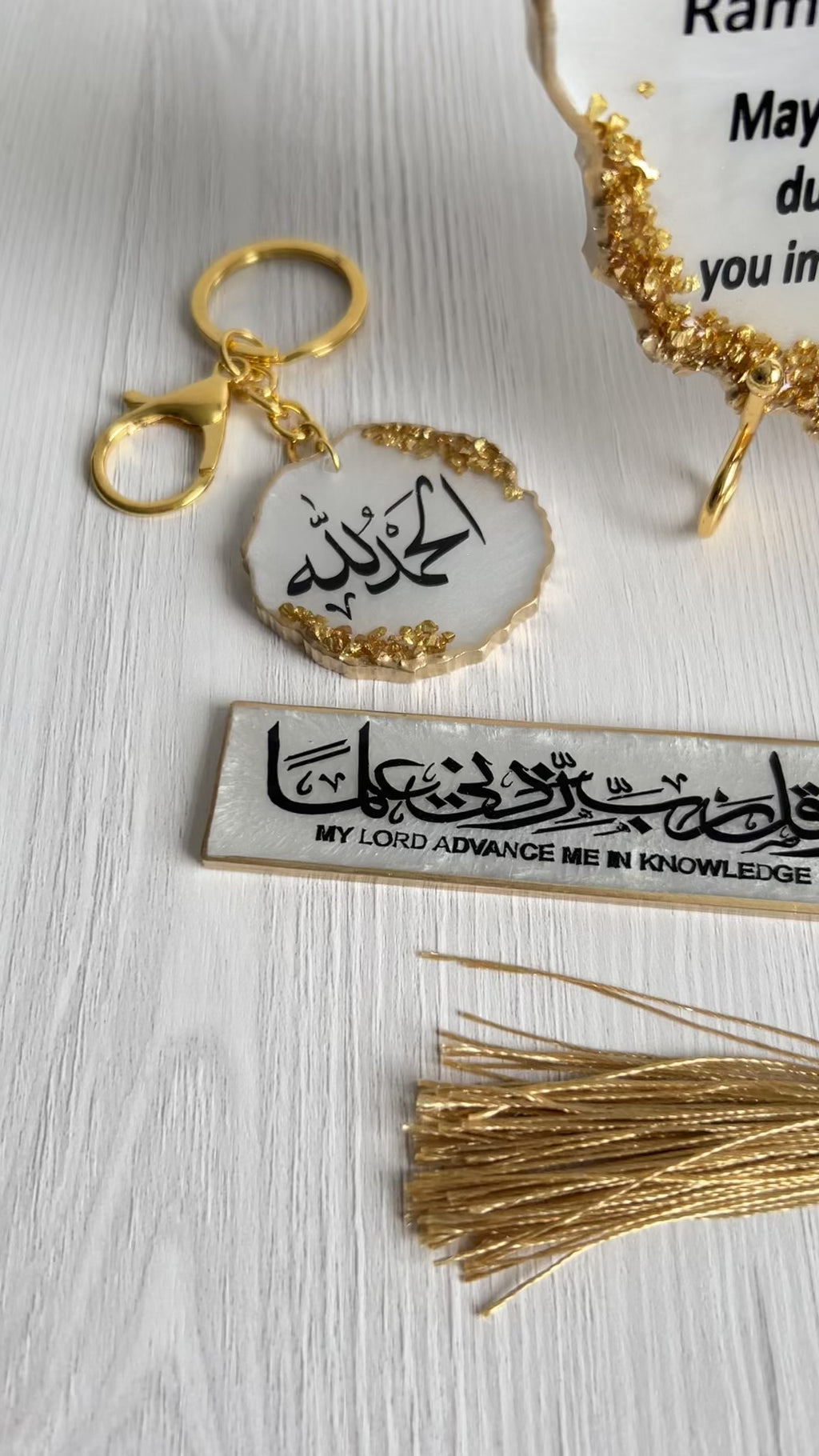 A resin plaque with gold crushed glass detailing, personalized with 'Itikaf Mubarak' and some Arabic text, accompanied by a candle, bookmark and a keychain with matching design, displayed alongside purple flowers.