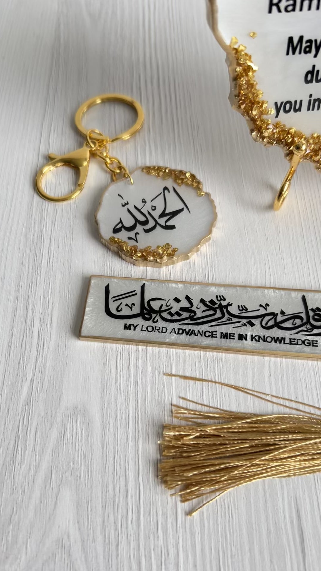 A resin plaque with gold crushed glass detailing, personalized with 'Itikaf Mubarak' and some Arabic text, accompanied by a candle, bookmark and a keychain with matching design, displayed alongside purple flowers.
