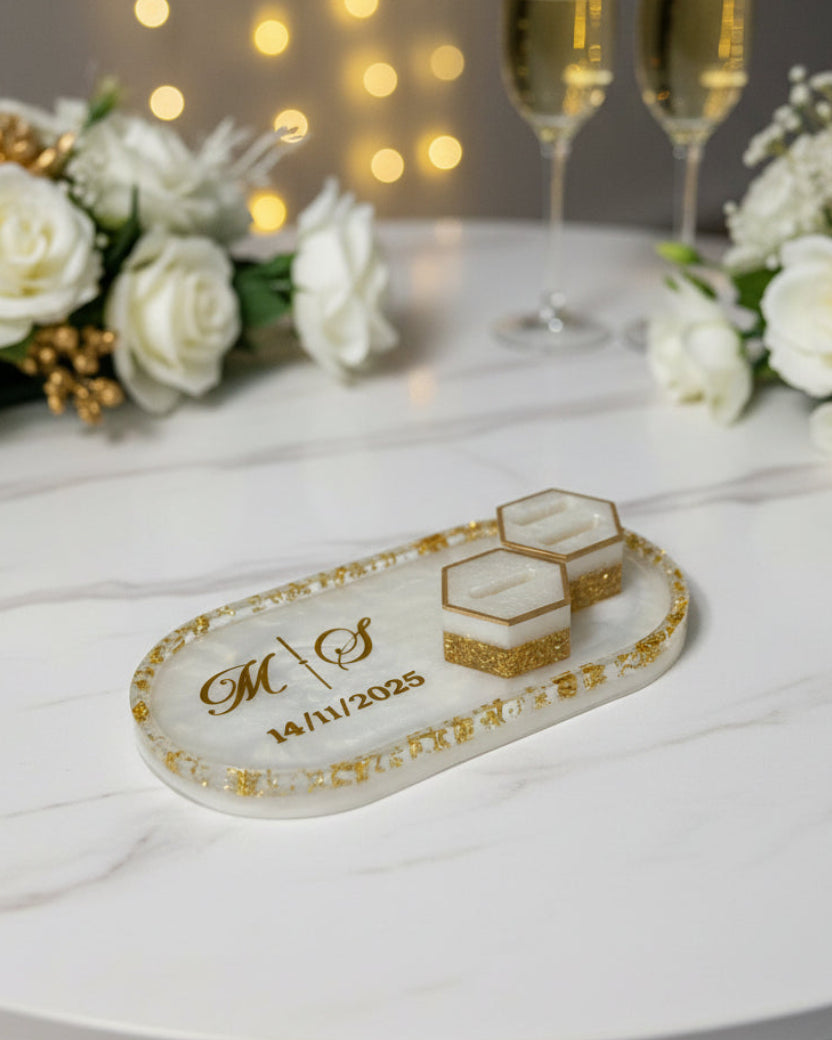Decorative tray with initials and year, flanked by champagne glasses and flowers on a table with string lights in the background.