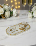 Decorative tray with initials and year, flanked by champagne glasses and flowers on a table with string lights in the background.